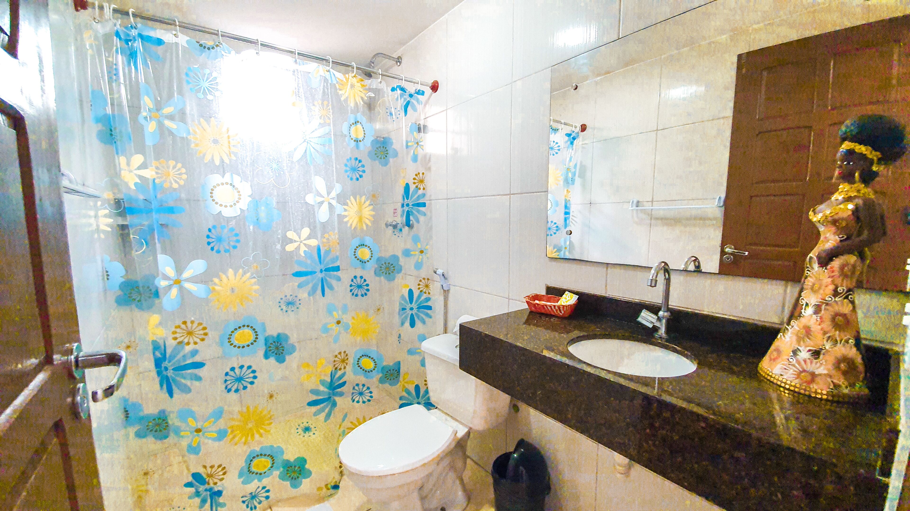 Casa de banho com cortina de chuveiro estampada com flores, pia com espelho em cima e sanita.