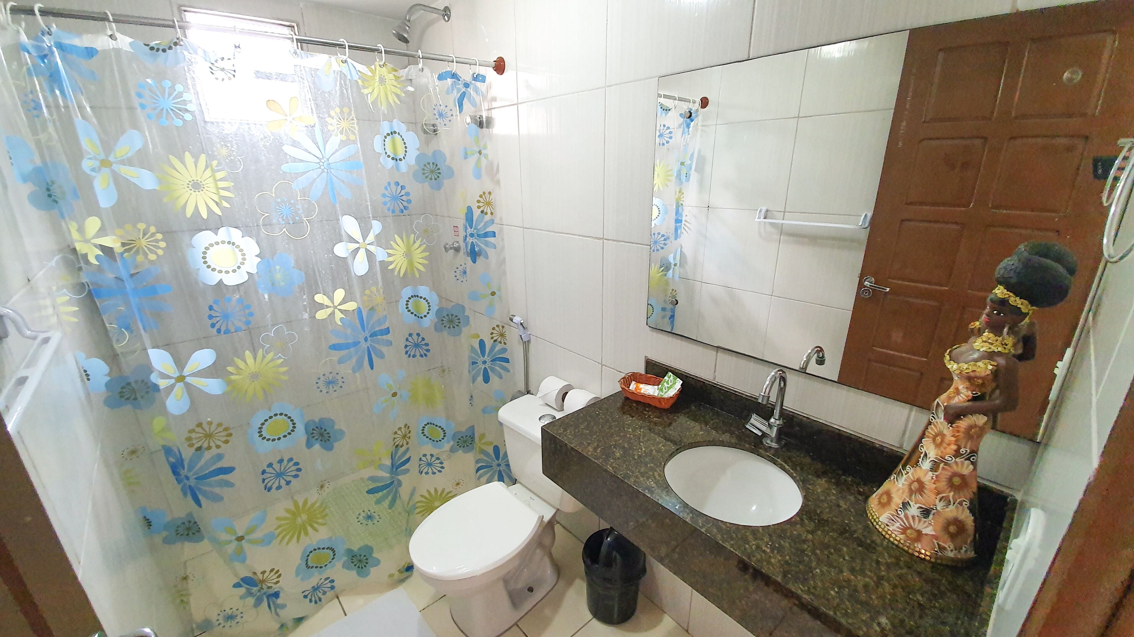 Un baño con inodoro, lavabo, cortina de ducha con motivos florales y un espejo.