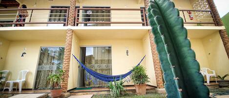 A building with a balcony, a hammock, and a large cactus.