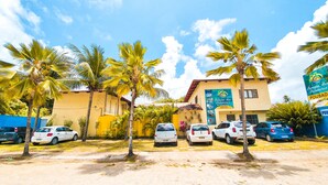 A hotel with a yellow facade, parked cars, and palm trees in the foreground. - Pousada Paraíso das Palmeiras (Paripueira)