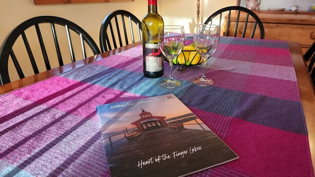 A table set with a bottle of red wine, two wine glasses, and a placemat with a book titled "Heart of the Finger Lakes". - Wonderful Quiet neighborhood retreat in the Village of Watkins Glen (Watkins Glen)