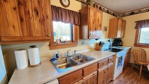 A kitchen with wooden cabinets, a double sink, and a window with a view of trees. - Wonderful Quiet neighborhood retreat in the Village of Watkins Glen (Watkins Glen)