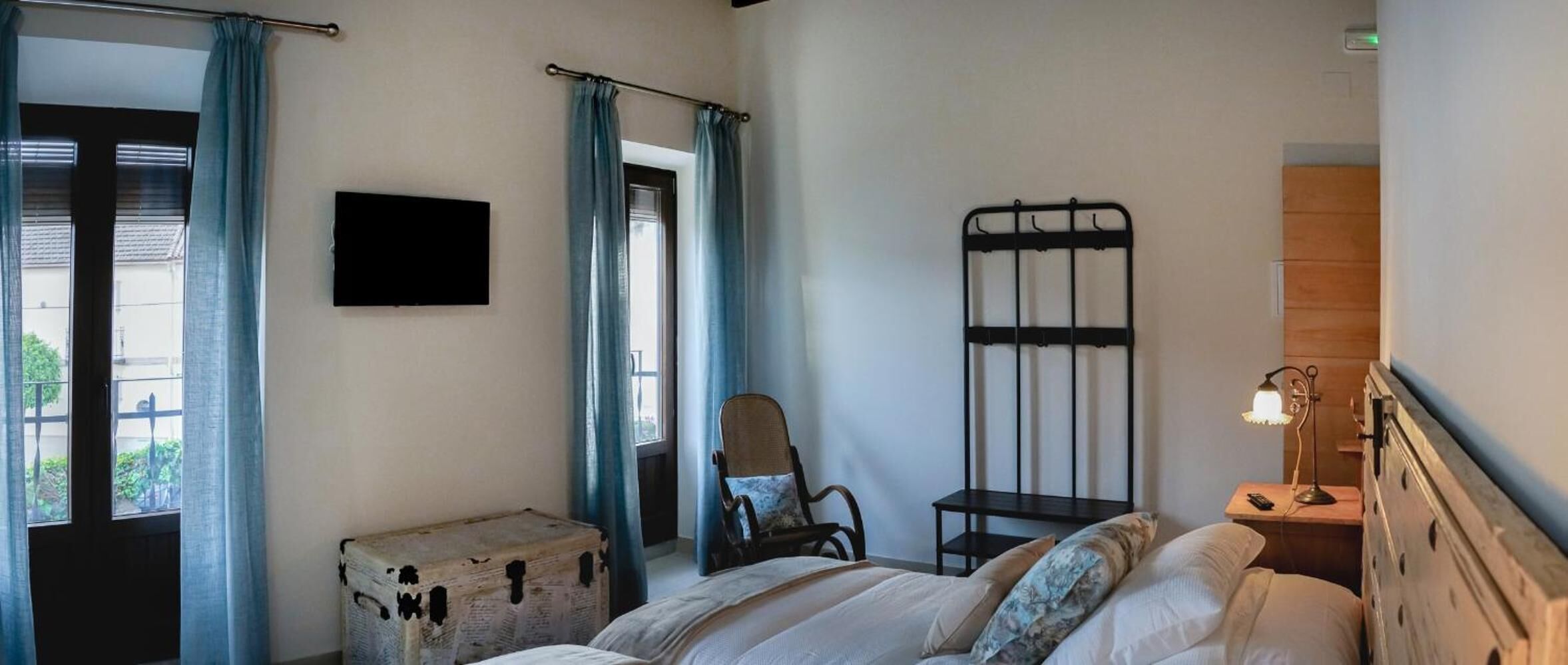 Une chambre à coucher avec un lit, une chaise, une petite table, une valise et un téléviseur fixé au mur.