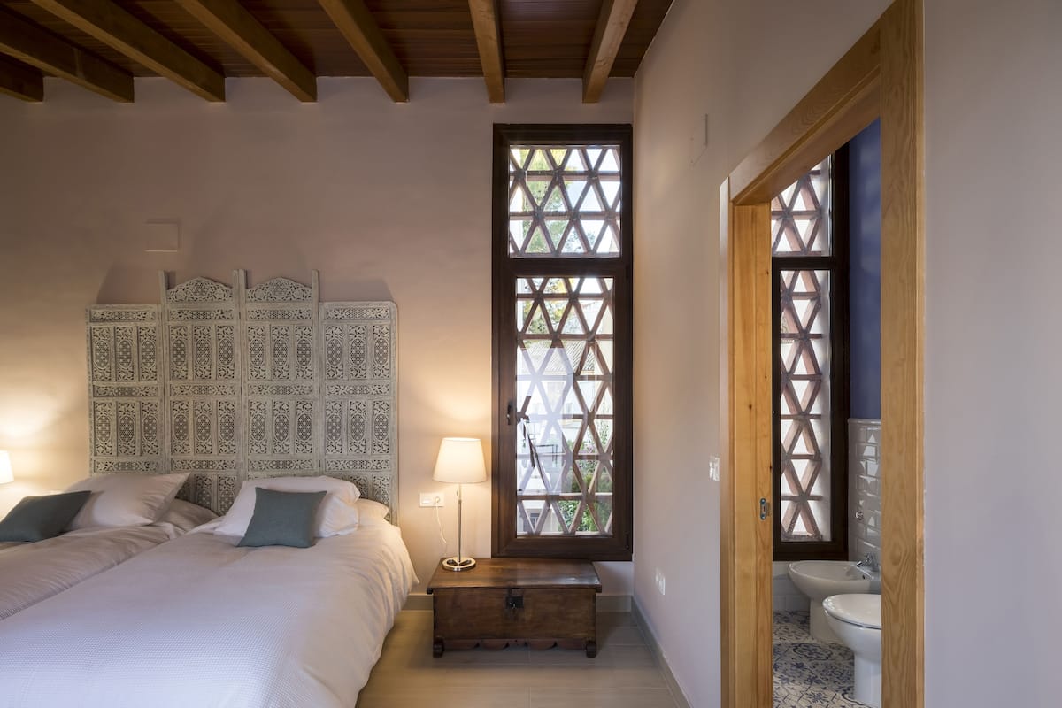 Une chambre à coucher avec un lit, des lampes de chevet, une table de chevet et une fenêtre ornée d’un motif en treillis.