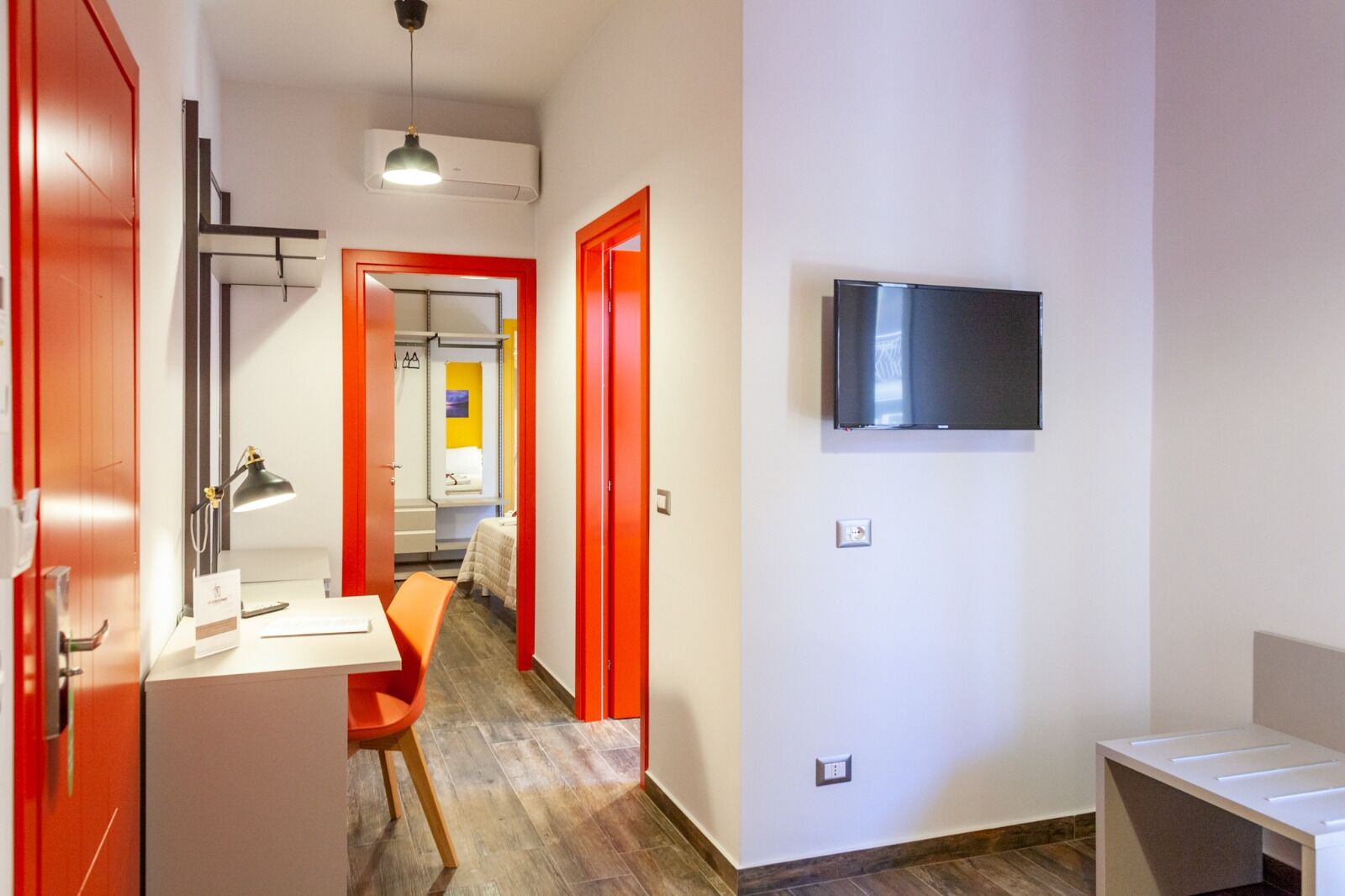 Una camera d'albergo moderna con una televisione a schermo piatto montata a parete, una scrivania con una lampada e una sedia.
