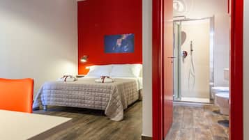 A hotel room with a bed, a red accent wall, a shower area, and a white toilet.