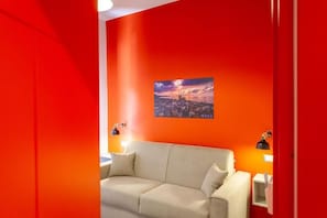 A room with a red wall, a beige sofa, and a cityscape picture. - Five Rooms Brolo (Brolo)