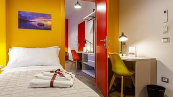 A hotel room with a bed, a desk, a chair, and a desk lamp.