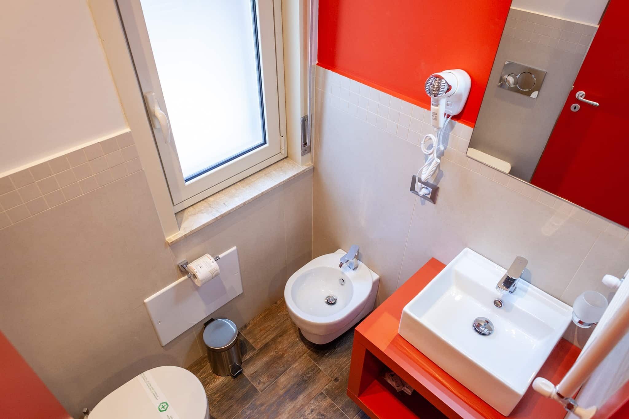 A bathroom with a toilet, bidet, sink, and a window.