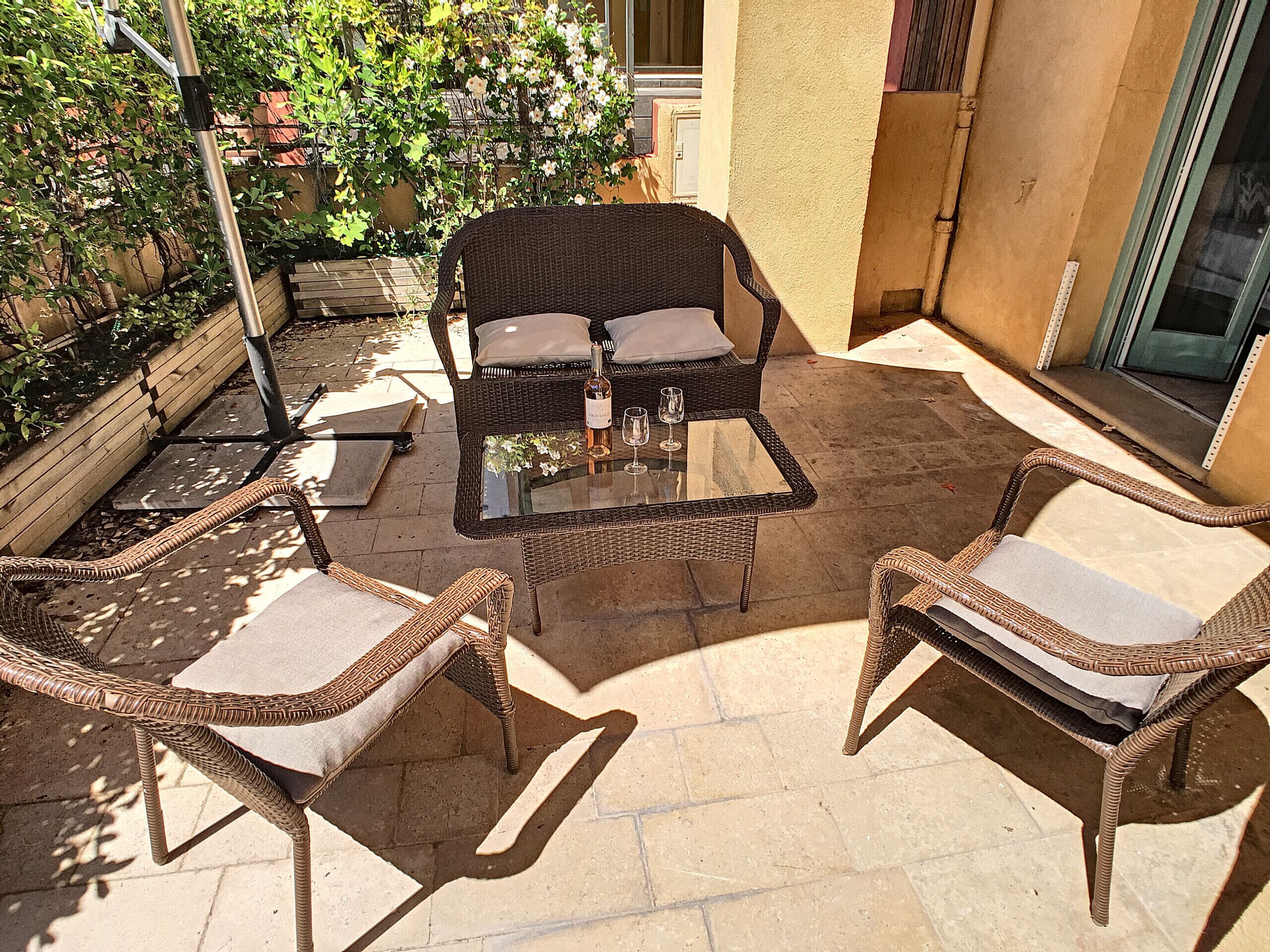 A patio with wicker furniture, a glass table, and a bottle of wine.