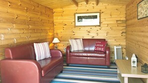 A cozy room with wooden walls, a red leather sofa, a striped rug, and a framed picture on the wall. - 3 bedroom accommodation in Aberdaron (Aberdaron)