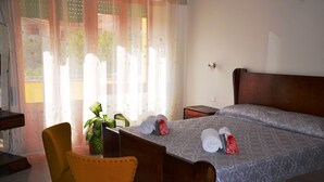A hotel room with a bed, a desk, a chair, and a potted plant.