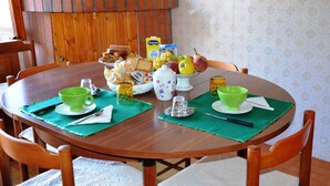 A wooden dining table set with green placemats, a bowl of fruit, a pitcher, and a box of milk.