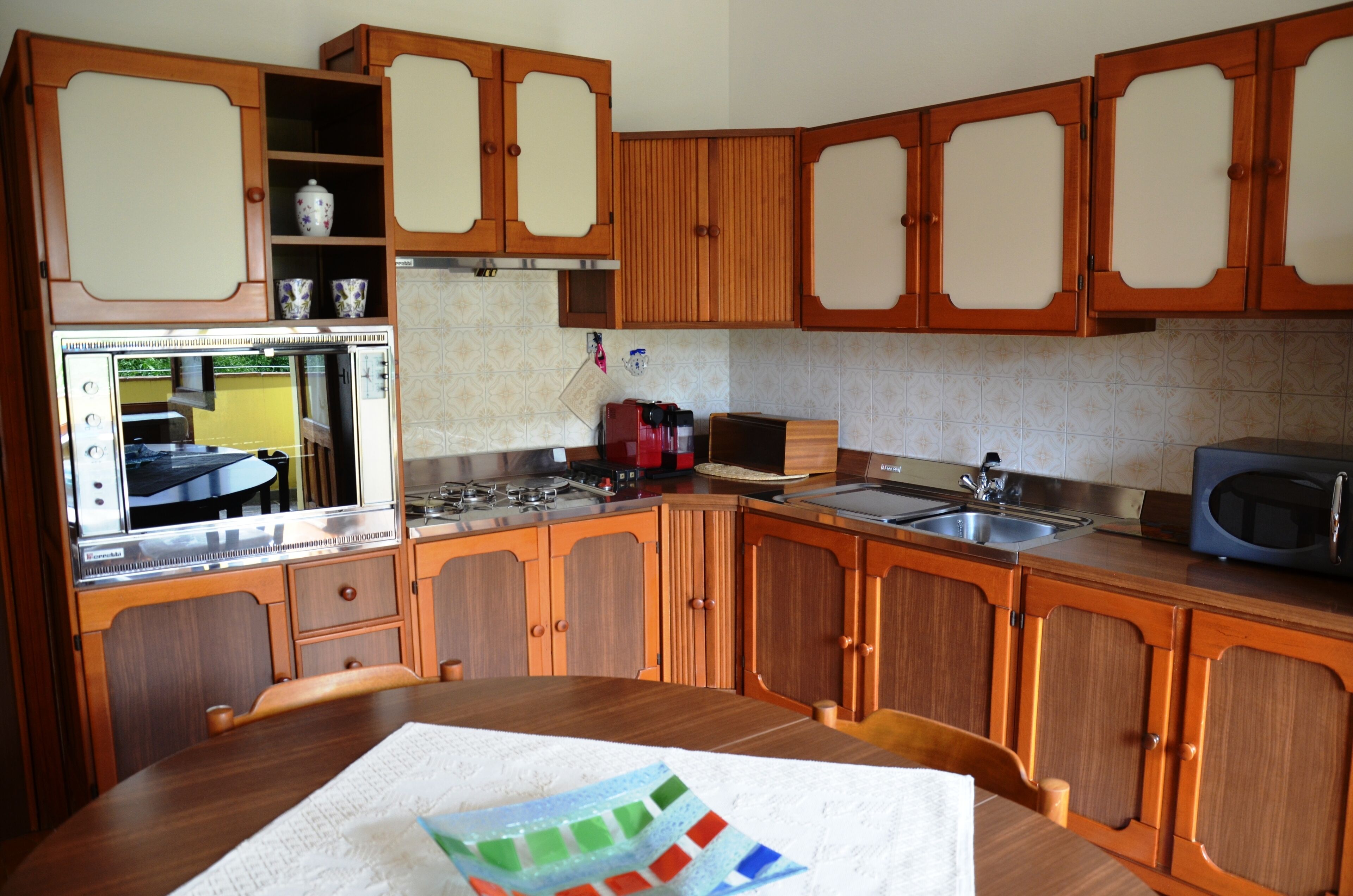 Una cocina con gabinetes de madera, estufa, pileta y microondas.