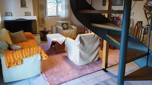 A cozy living room with a fireplace, a sofa, a coffee table, and a spiral staircase. - Plataniotissa Mansion (Plataniotissa)