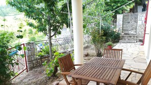 A wooden table and chairs set on a stone patio with a view of a stone wall and greenery. - Plataniotissa Mansion (Plataniotissa)