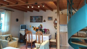 A cozy living room with wooden beams, a dining table with chairs, a TV, and a staircase. - Plataniotissa Mansion (Plataniotissa)