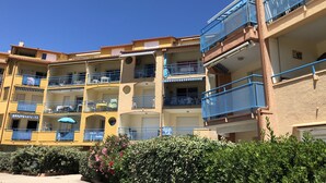 Un edificio residencial de varios pisos con balcones, cielo despejado y seto bien cuidado.