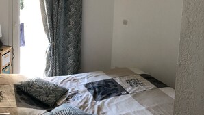 Un dormitorio con una cama, cortinas estampadas, una lámpara colgante y un ventanal pequeño.