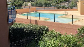 Una piscina con una barrera de seguridad de malla, rodeada de follaje y vista al mar.