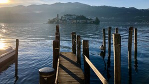Un muelle de madera se extiende sobre aguas tranquilas, con una vista distante de un asentamiento en la ladera.