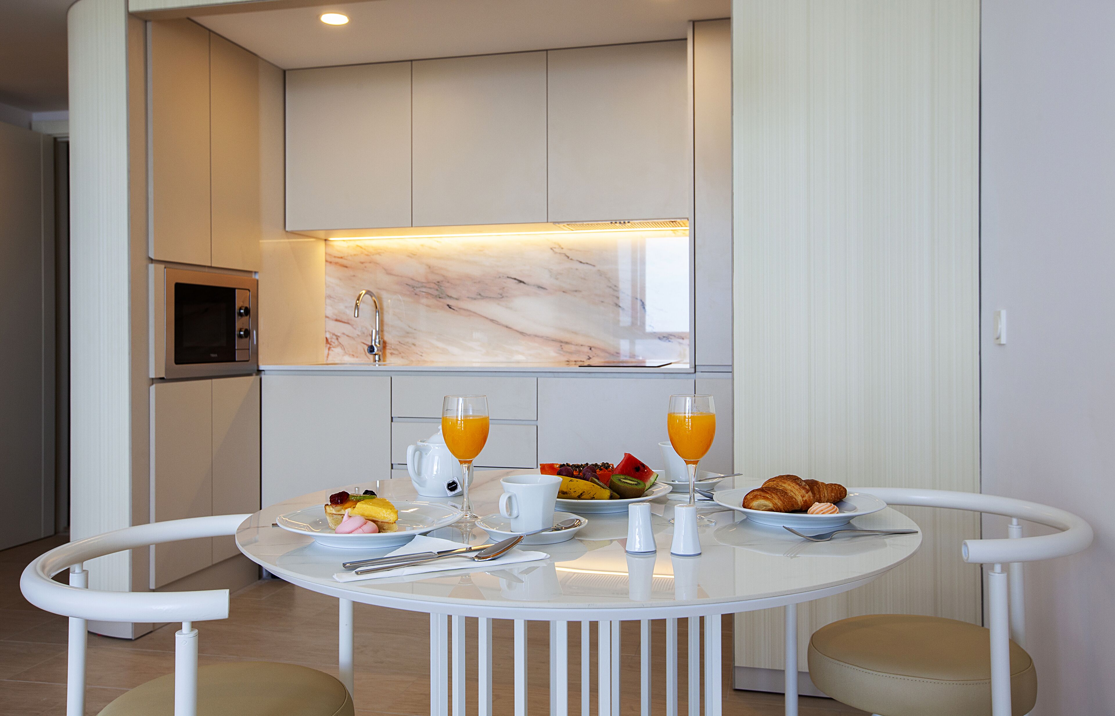A modern kitchen with a white marble backsplash, a built-in microwave, and a dining area with a white table and chairs.