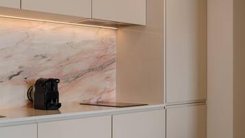 A kitchen with a marble backsplash, a coffee maker, and a white countertop.