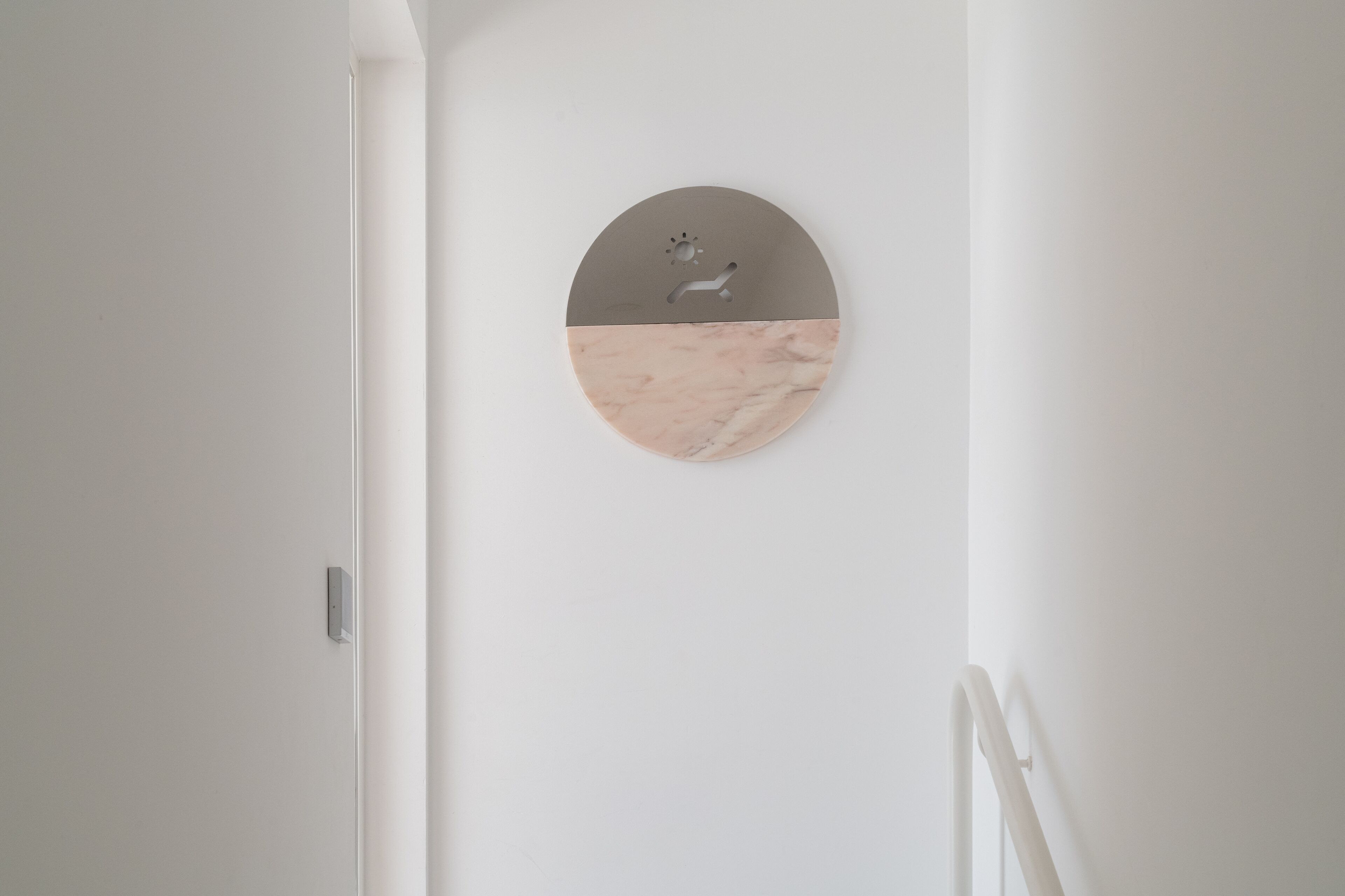 A minimalist bathroom with a white wall, a round mirror with a marble-like texture, and a simple faucet.