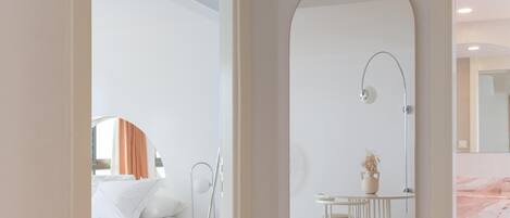 A modern hotel room with a large mirror, a bed, a bedside table, and a small seating area.