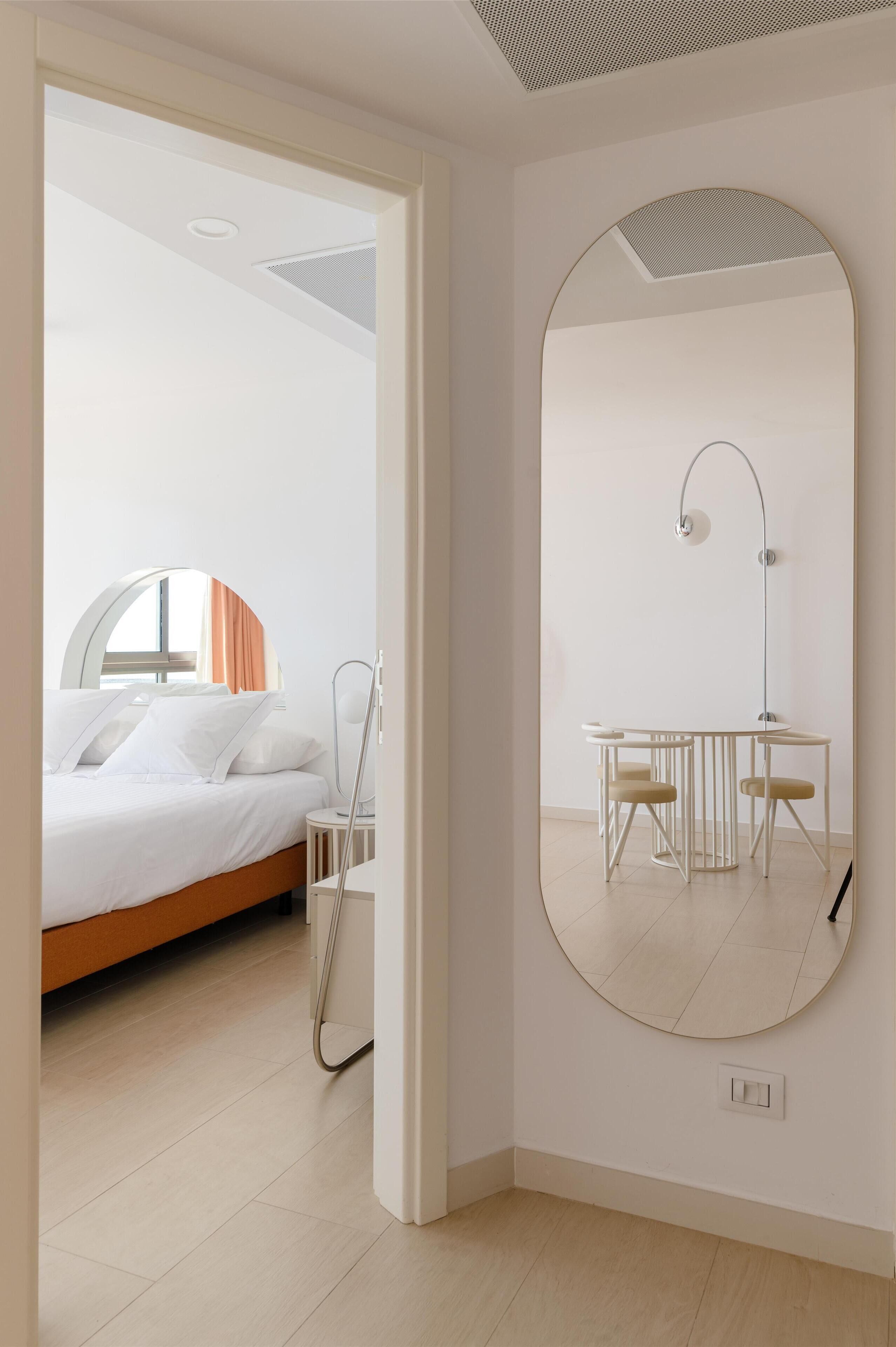 Una habitación de hotel moderna con una cama, un espejo redondo, un escritorio con dos sillas y una ventana con cortinas.