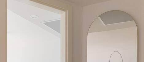 Una habitación de hotel moderna con una cama, un espejo redondo, un escritorio con dos sillas y una ventana con cortinas.