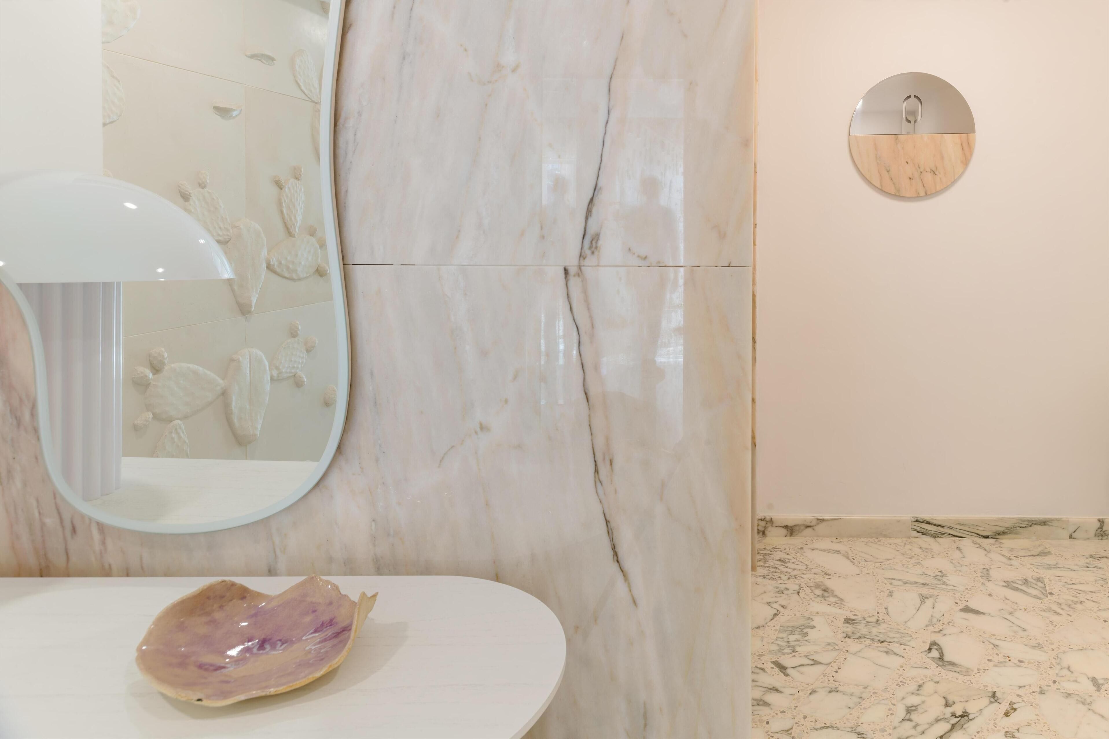 A bathroom with a marble wall, a round mirror, and a sink with a decorative item.