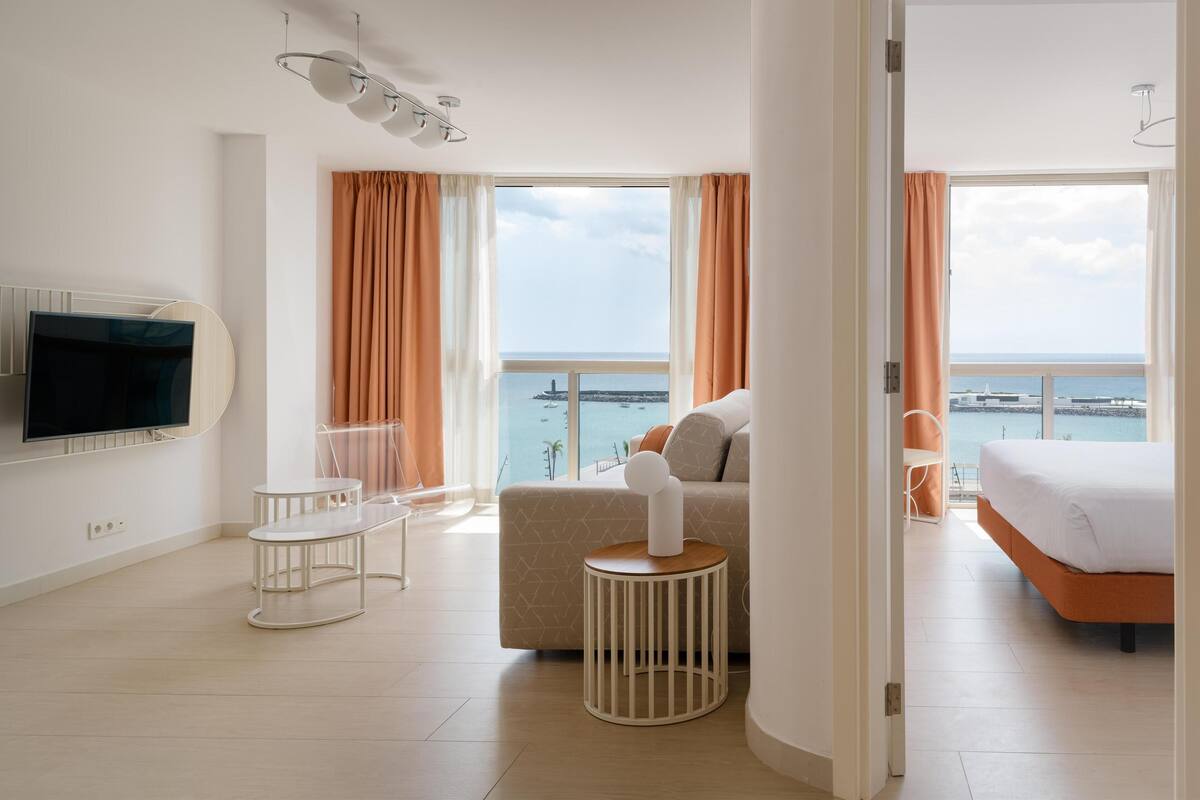 Ein modernes Hotelzimmer mit großem Fernseher, einer Couch, einem Bett und einem Balkon mit Meerblick.