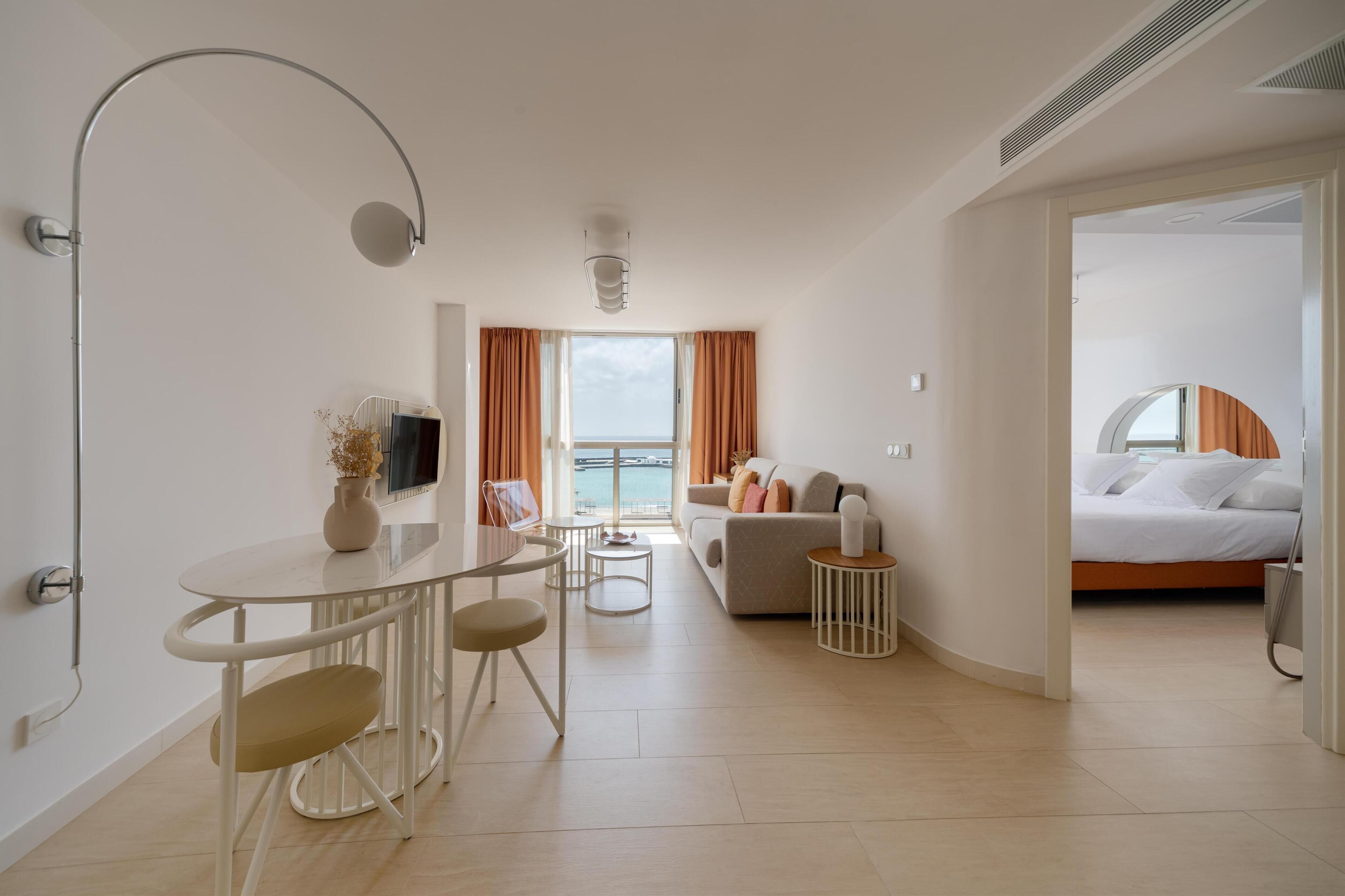 A modern hotel room with a dining area, a sofa, and a bed.