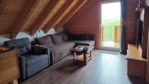 A loft-style room with a wooden ceiling, a sofa, a small table, and a television.