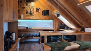 A wooden interior with a kitchen area, a dining table, and a high ceiling with wooden beams.