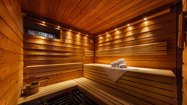 Una sauna de madera con bancos, un banco con una toalla y un cuenco de piedra.