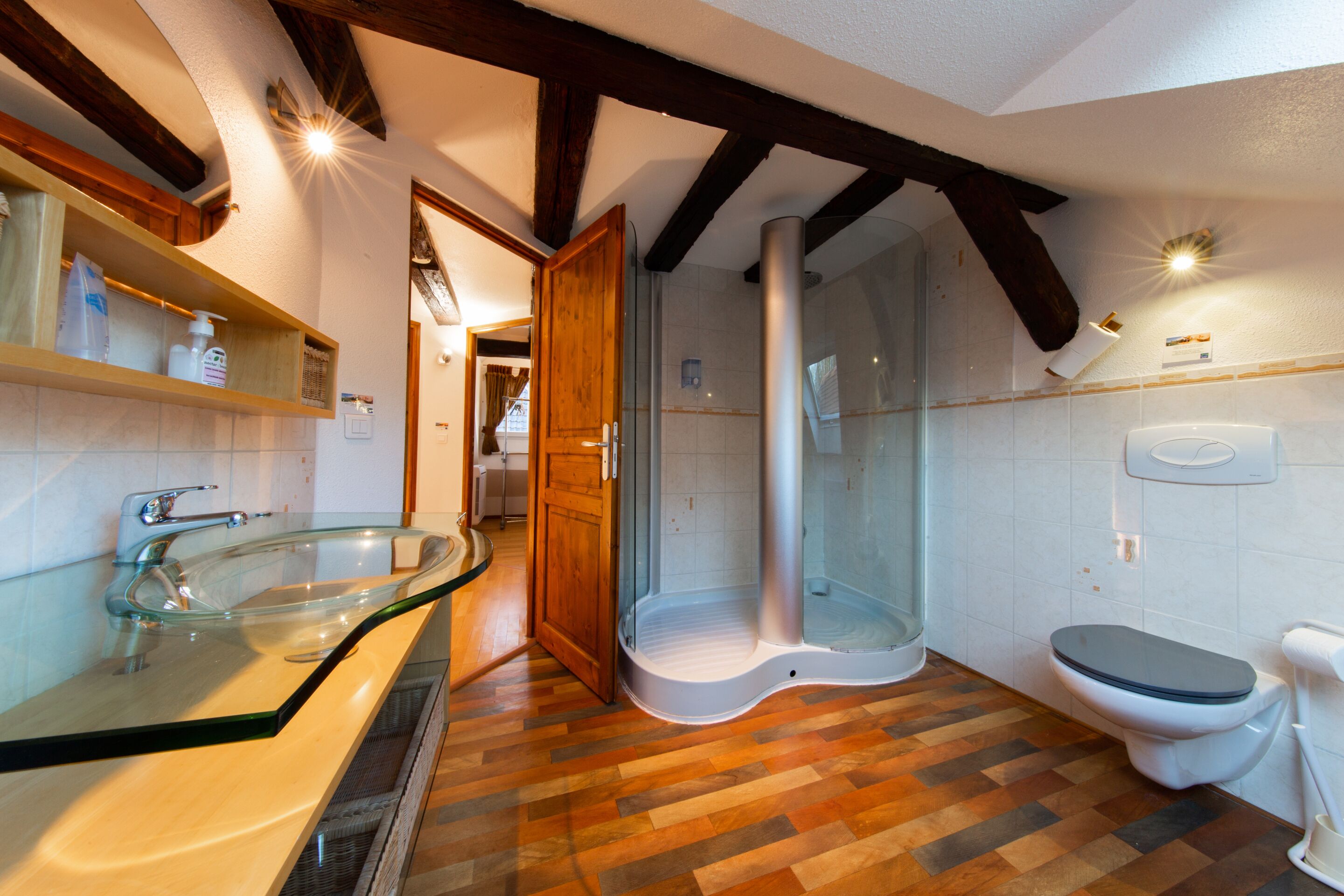 Een badkamer met een glazen douchecabine, toilet en een wastafel met een houten blad.