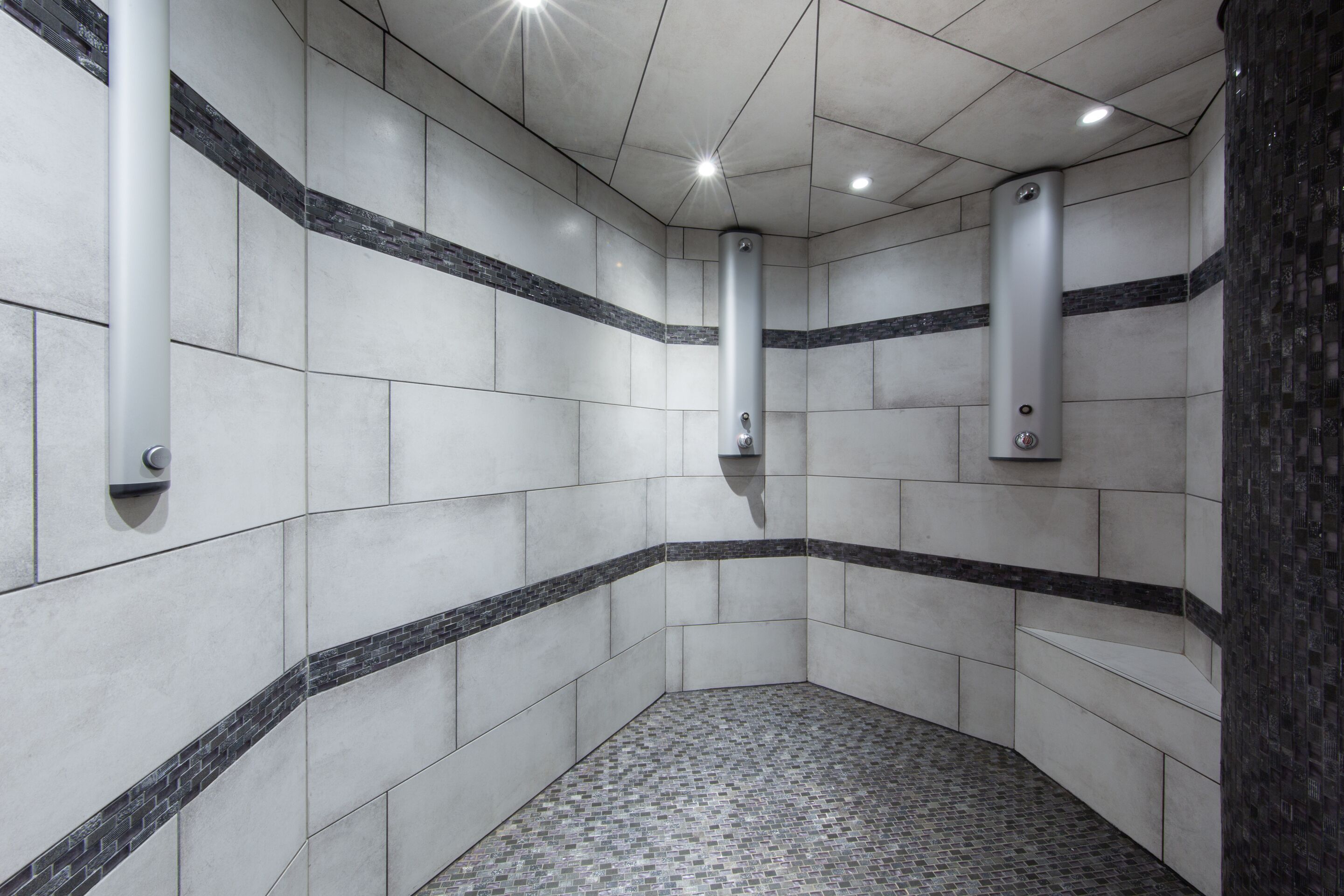 Un coin de toilettes avec des murs carrelés, un sol à motifs et deux éléments d’aménagement verticaux.
