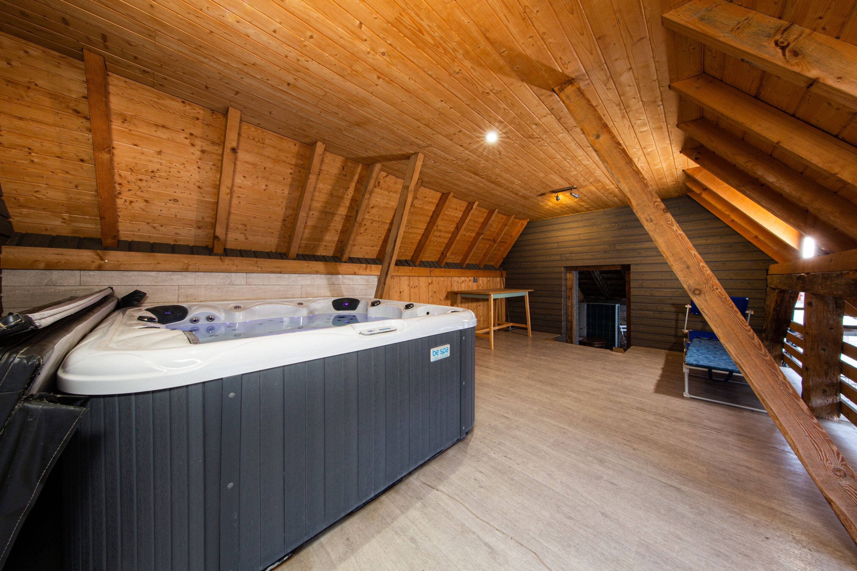 Een hottub in een houten chalet met schuine daklijn en een kleine tafel.