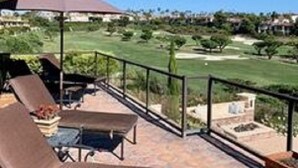 En terrasse med loungesenge og et bord, med udsigt over en golfbane.