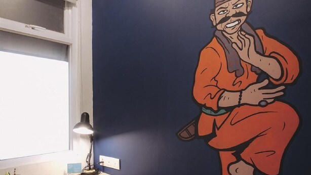 A room with a desk, a chair, a lamp, and a wall mural.