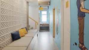 A hallway with a patterned wall, a seating area with cushions, and a mural of a person.