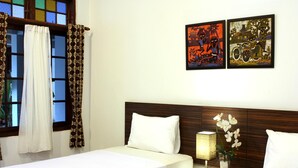 A hotel room with two beds, a wooden headboard, a nightstand with a lamp, and two framed artworks on the wall. - Grand Marto Hotel (Yogyakarta)