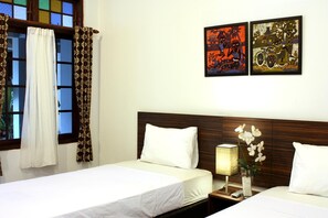 A hotel room with two beds, a wooden headboard, a nightstand with a lamp, and two framed artworks on the wall. - Grand Marto Hotel (Yogyakarta)