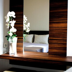 A mirror reflecting a bed, a white pillow, and a vase with white flowers. - Grand Marto Hotel (Yogyakarta)