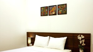 A hotel room with a wooden headboard, white bedding, a bedside lamp, and three framed artworks on the wall. - Grand Marto Hotel (Yogyakarta)