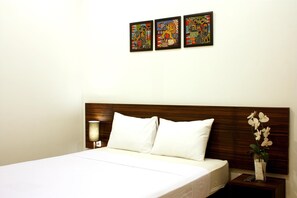 A hotel room with a wooden headboard, white bedding, a bedside lamp, and three framed artworks on the wall. - Grand Marto Hotel (Yogyakarta)