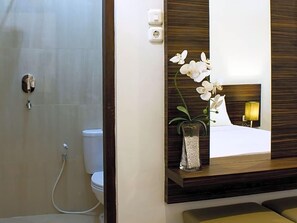 A bathroom with a shower, toilet, and a mirror with a bed reflection. - Grand Marto Hotel (Yogyakarta)