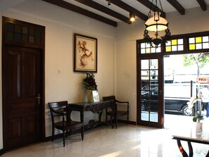 A reception area with a wooden door, a framed artwork, a table with chairs, and a large window with a view of the street. - Grand Marto Hotel (Yogyakarta)